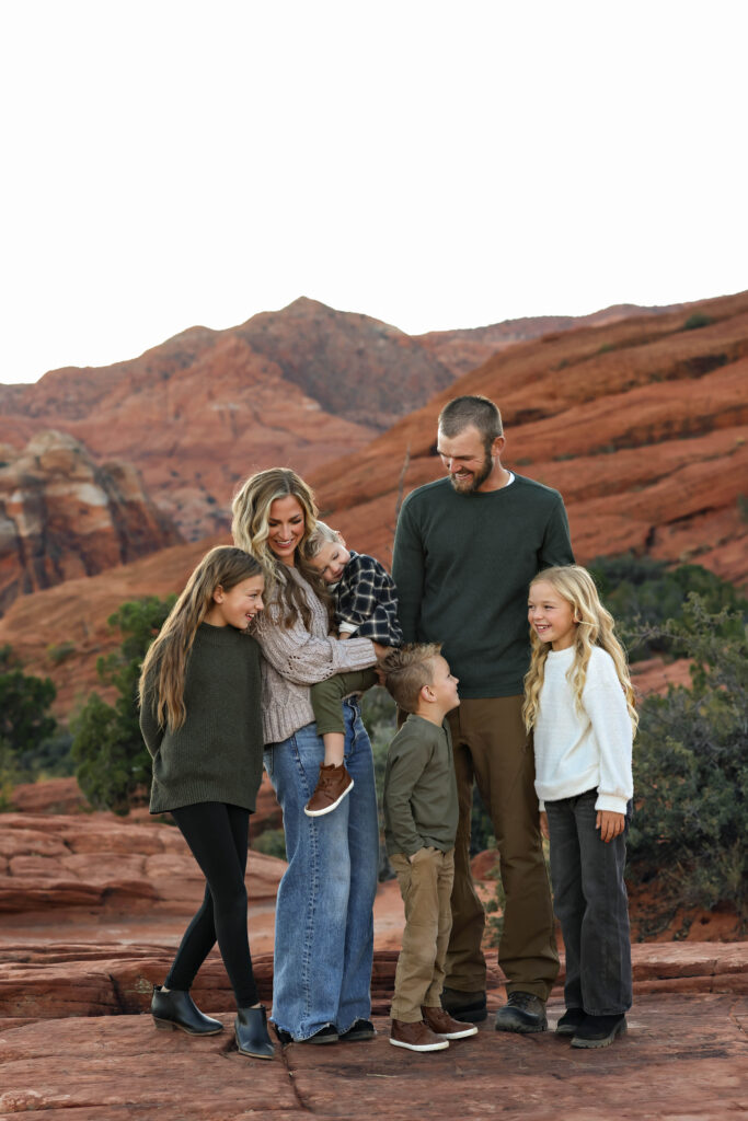 Family of six smiling during fall mini session in Southern Utah, surrounded by red rock and warm golden light.
