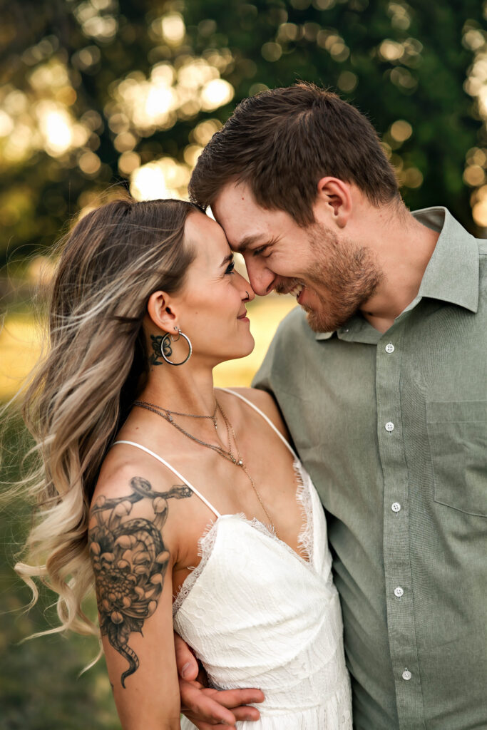A couple is snuggled up together in a beautiful green field with golden light. Dancing and playing during their family's fall mini session.