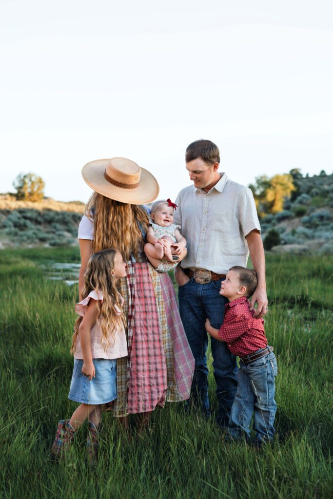 Family of 5 standing in green grass and playing together. Snuggled up and enjoying the early fall weather while they get their family pictures taken.