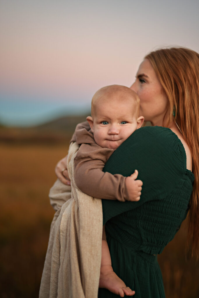 Mom holding baby in the beautiful evening light with a mountain sunset behind them on Cedar Mountain near Cedar City, Utah.