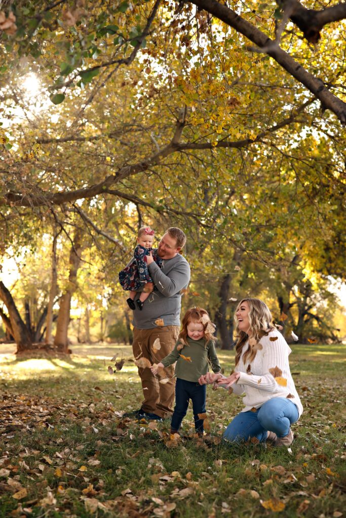 Family of four laughing and playing with the fallen leaves at Kirkland Fields in Washington, Utah, in the soft fall light.