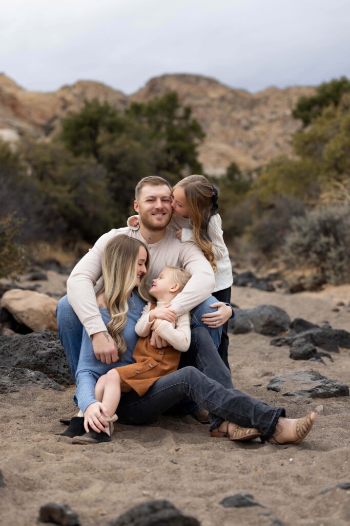 Family of four snuggled up together for a family photo in the sand of a dry river bank on the White Rocks trail at Snow Canyon State Park in Southern Utah.