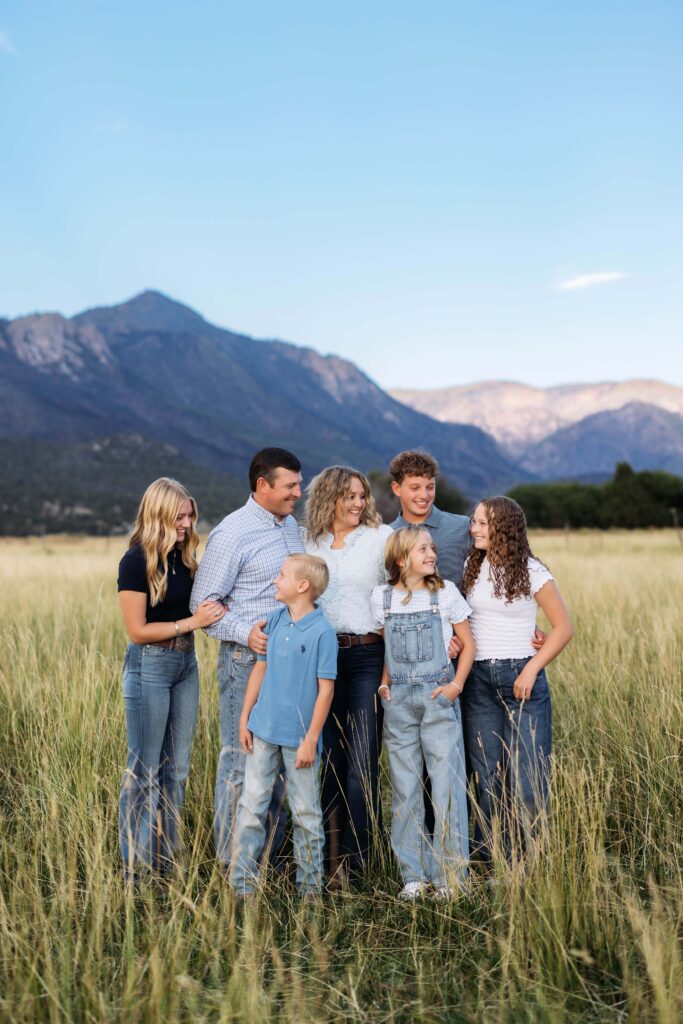 Family of seven standing and laughing in a field of tall yellow grass with beautiful mountain layers behind them in Pine Vally, Utah near St. George, Utah.