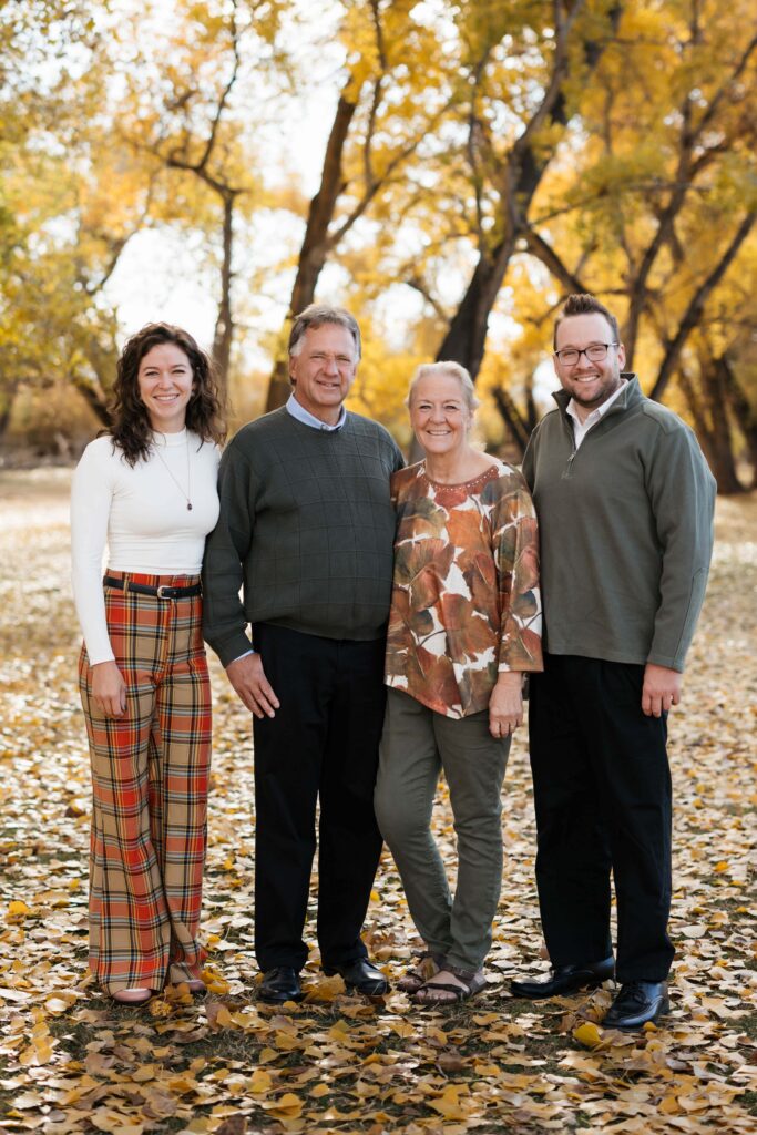 Family standing in a field with fallen yellow leaves and fall trees in the background at Kirkland Fields in Washington, utah.