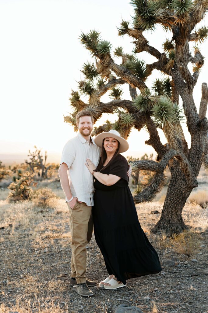 Couple standing together and smiling at the Joshua Tree National Monument near St. George, Utah in soft golden light against a beautiful desert landscape.