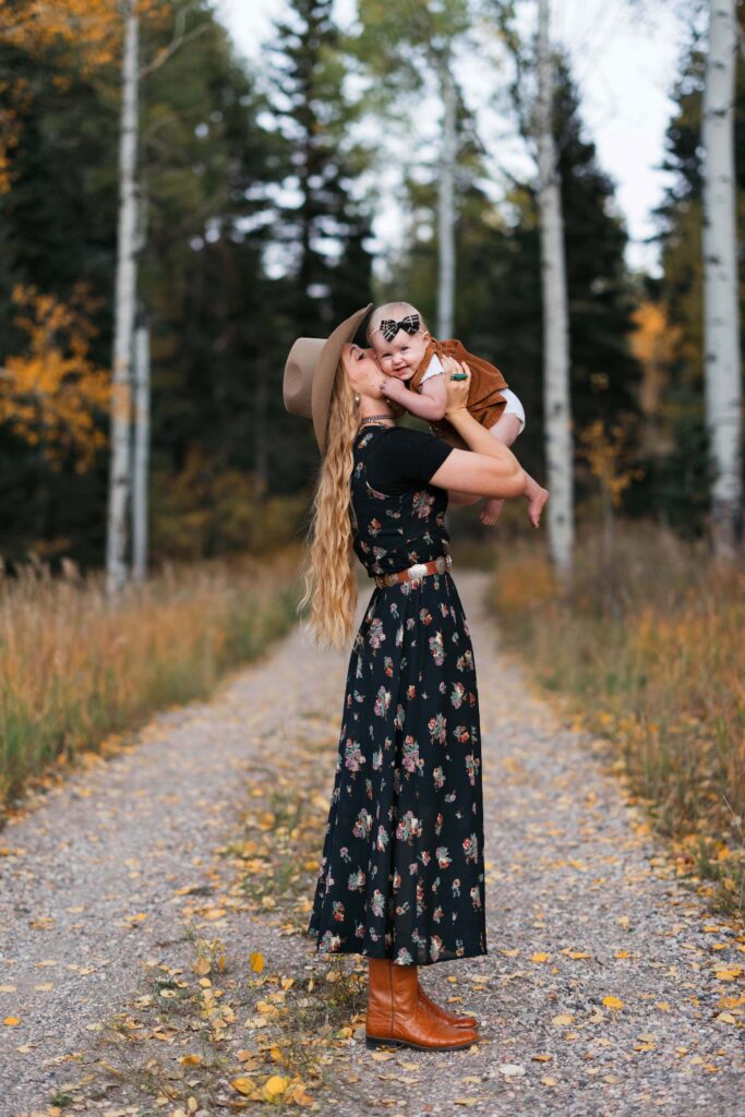 Mother holding her smiling baby on Cedar Mountain near Cedar City, Utah, surrounded by yellow aspens and pine trees, mountain scenery and soft fall light.
