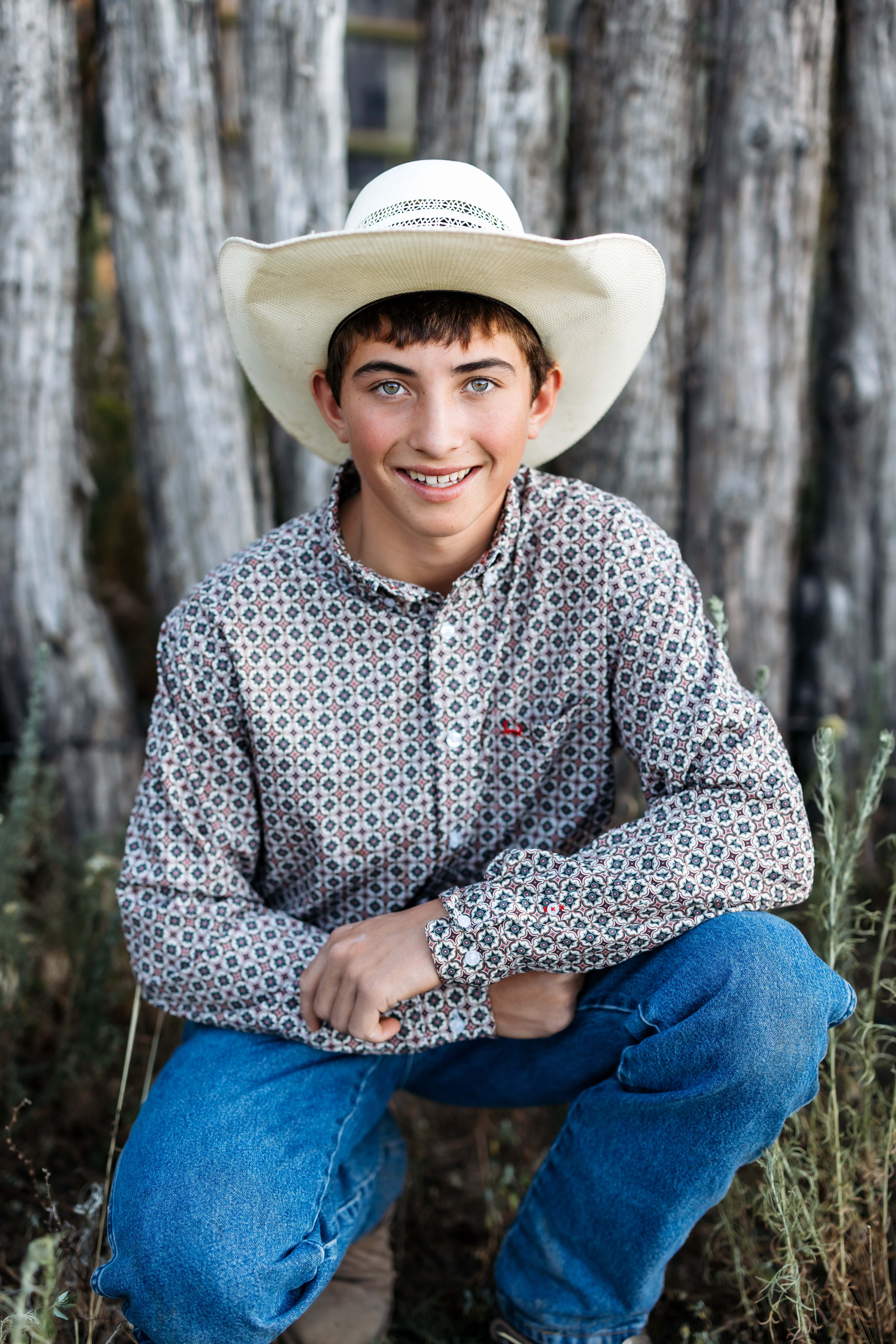A boy smiles for a senior portrait against a rustic wooden backdrop