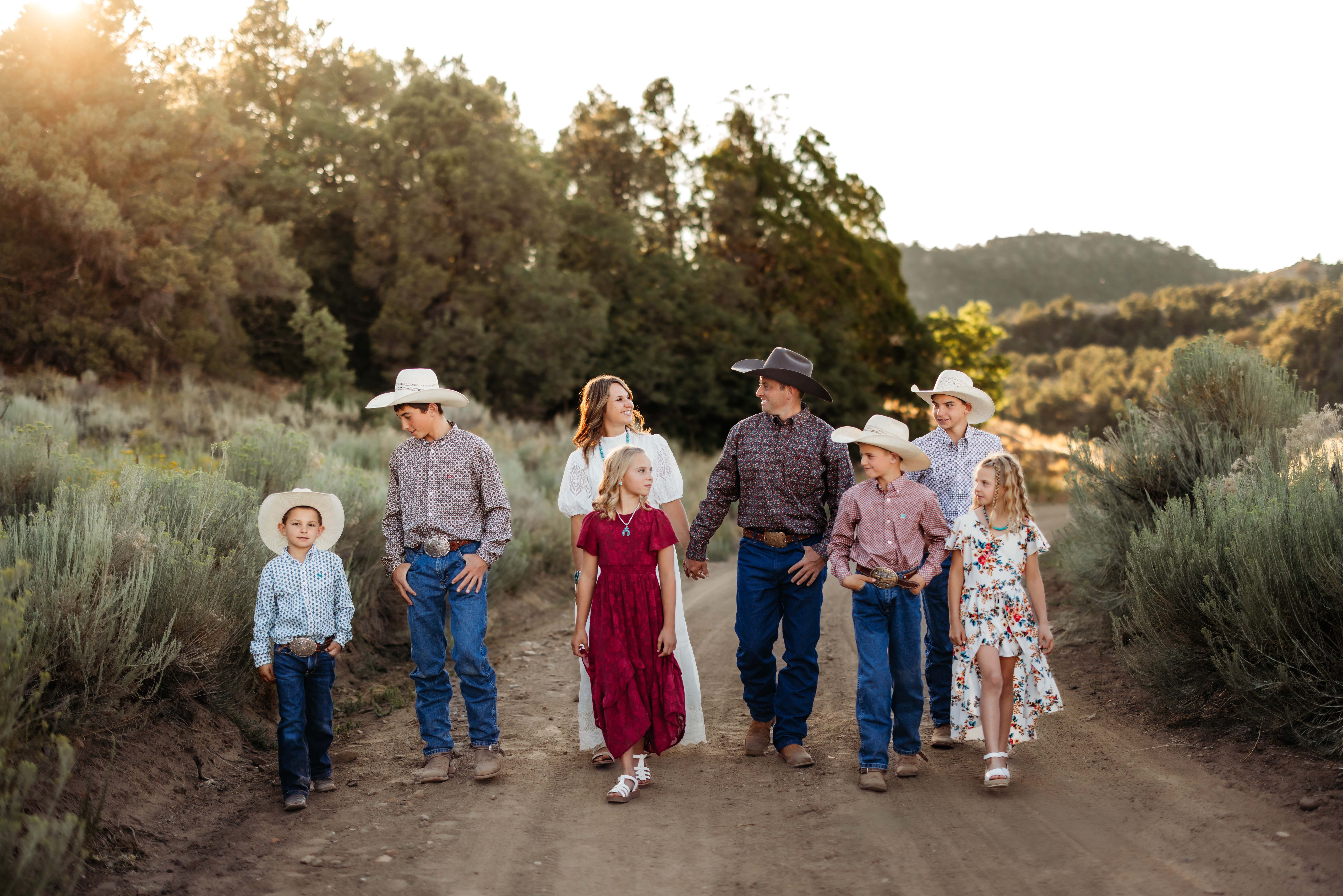 A family of eight walks down a dirt road with a beautiful desert mountain back drop and soft golden light