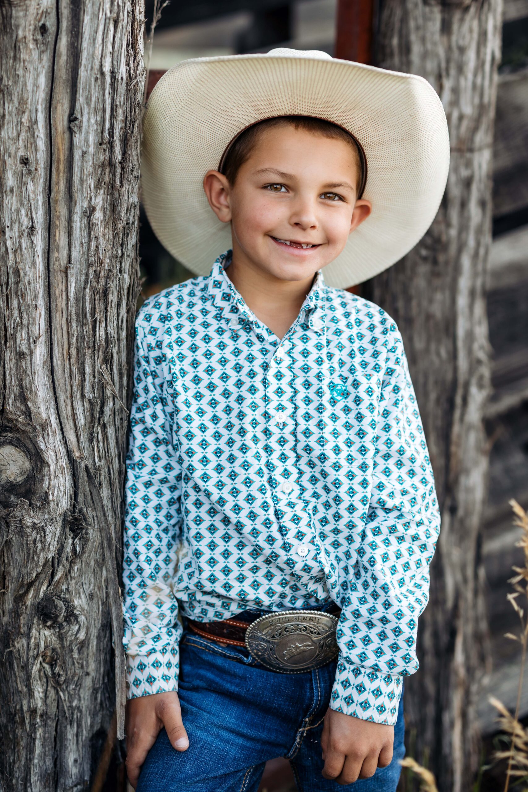 Cute cowboy wearing a hat and smiling for a portrait next to an old fence