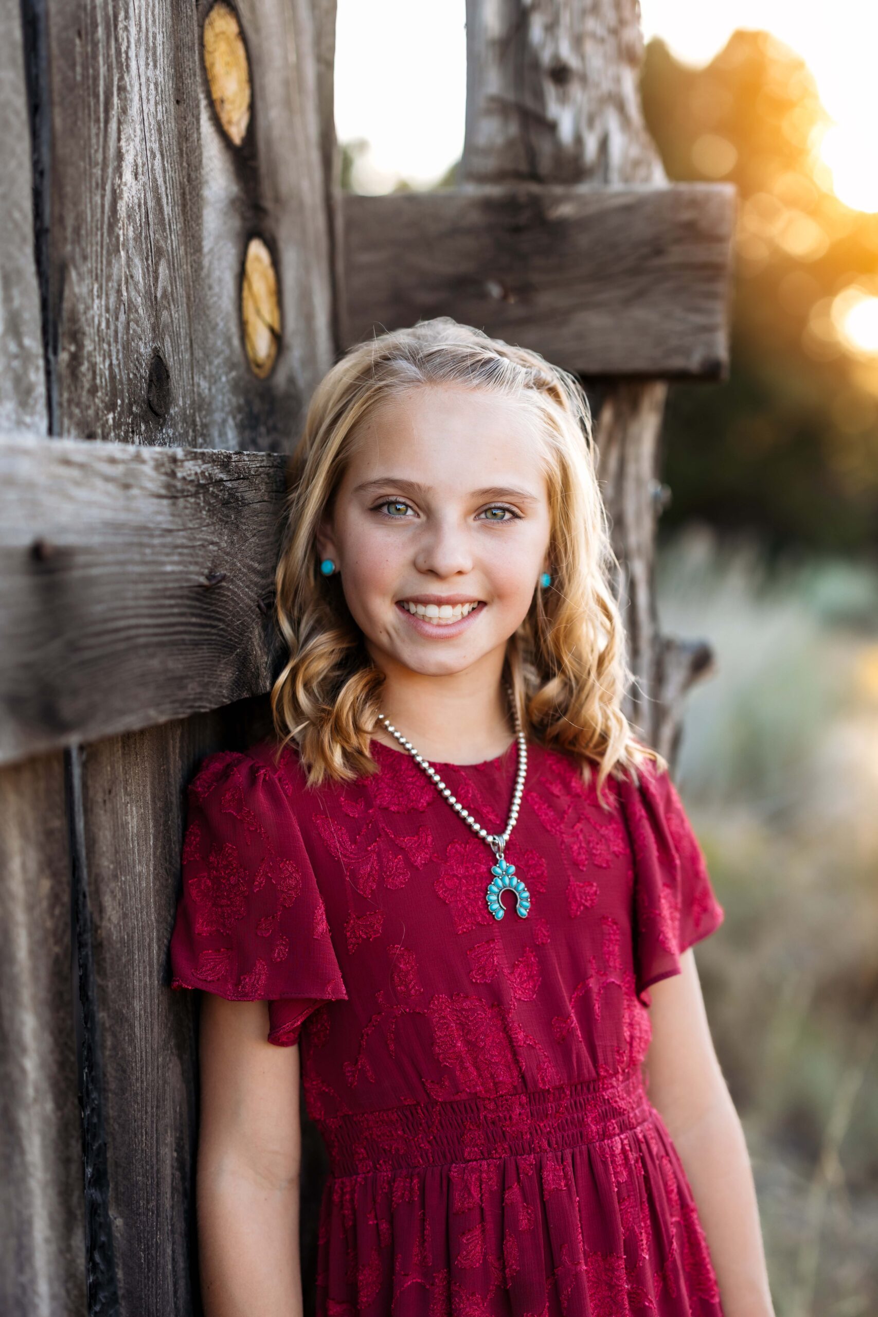 A girl looks and smiles for a photo session while wearing a red dress and turquoise jewelry