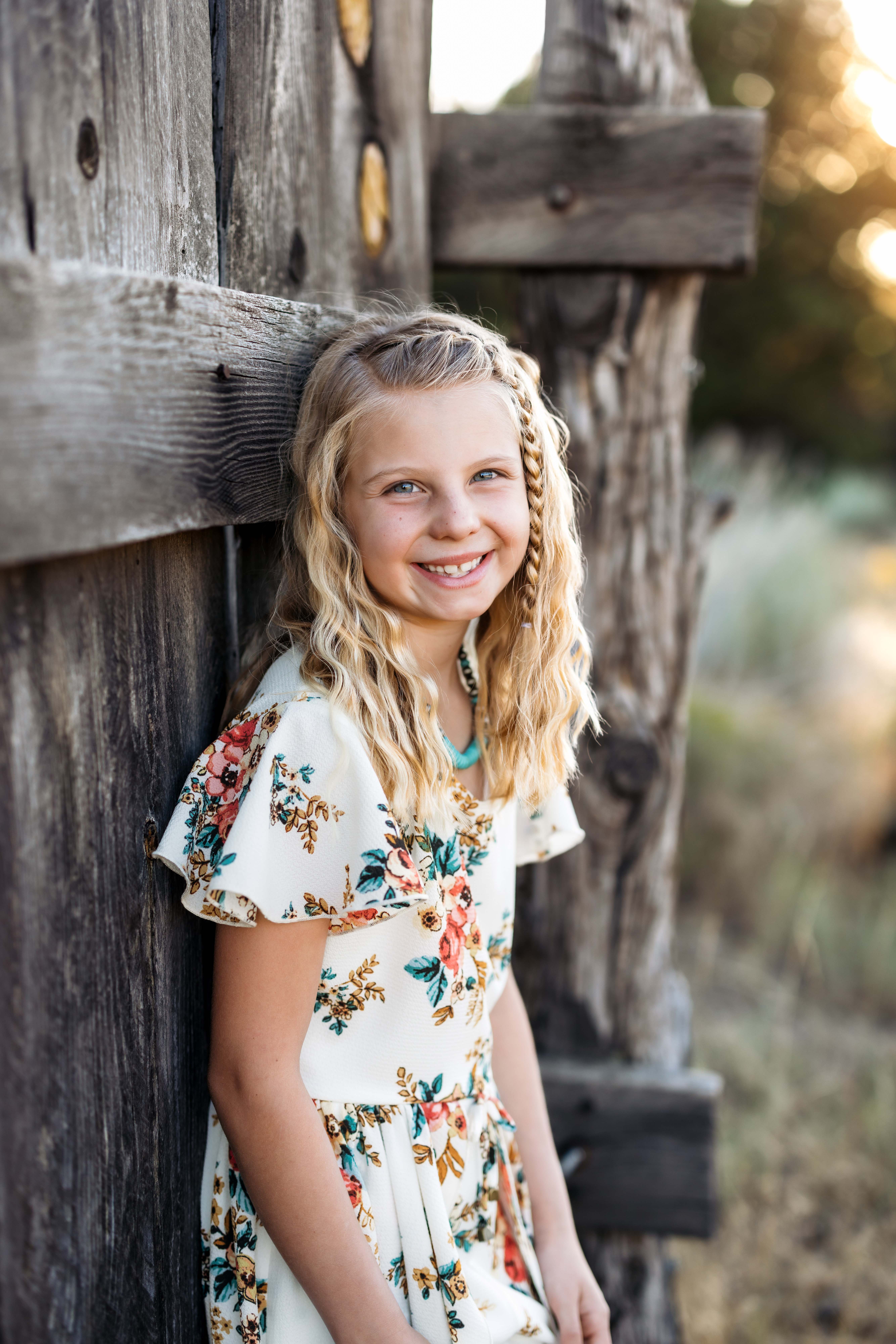 A girl stands against an old fence while smiling as the soft golden light glows behind her