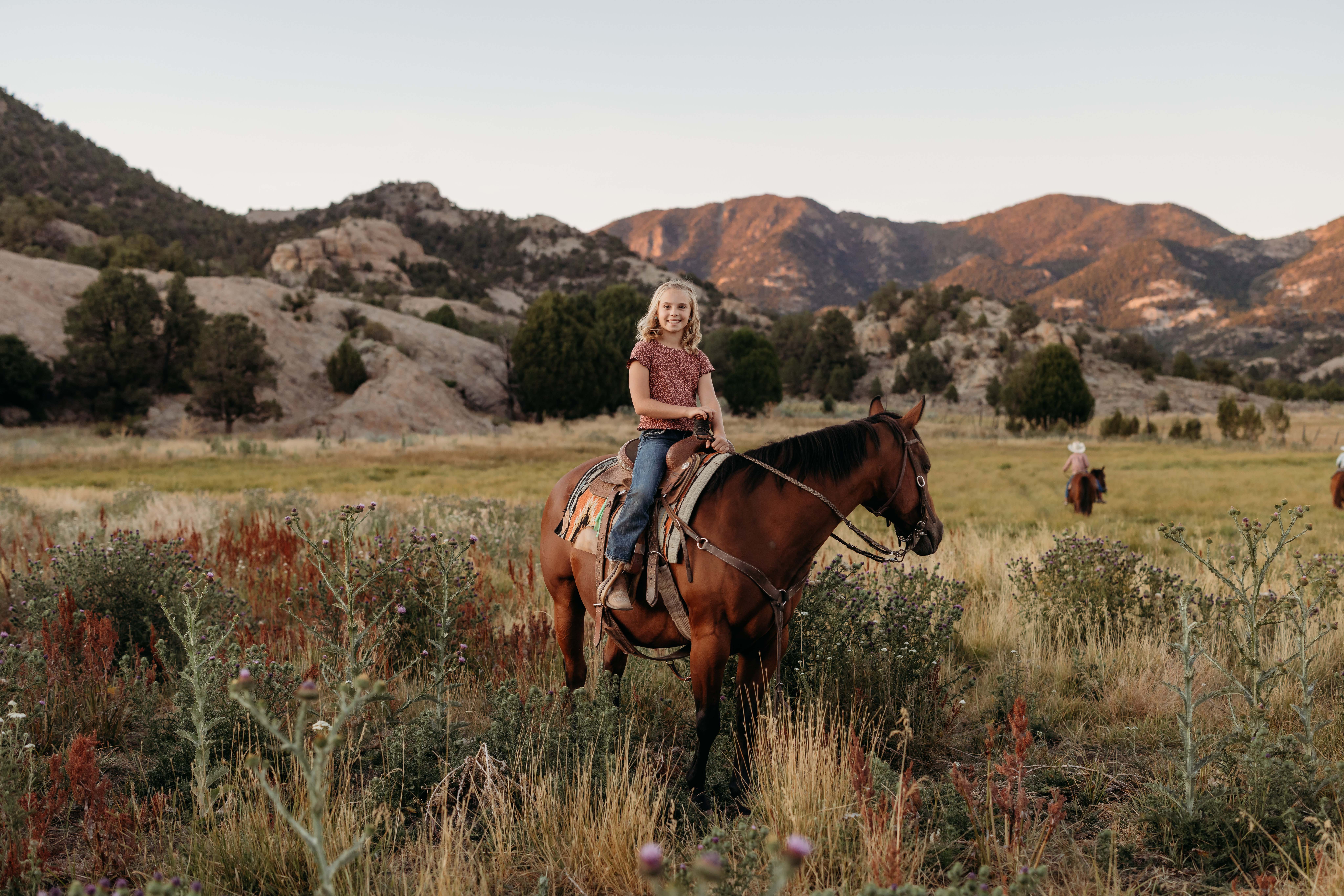 Girl sitting on horse in a beautiful green field with mountains and trees in the distance