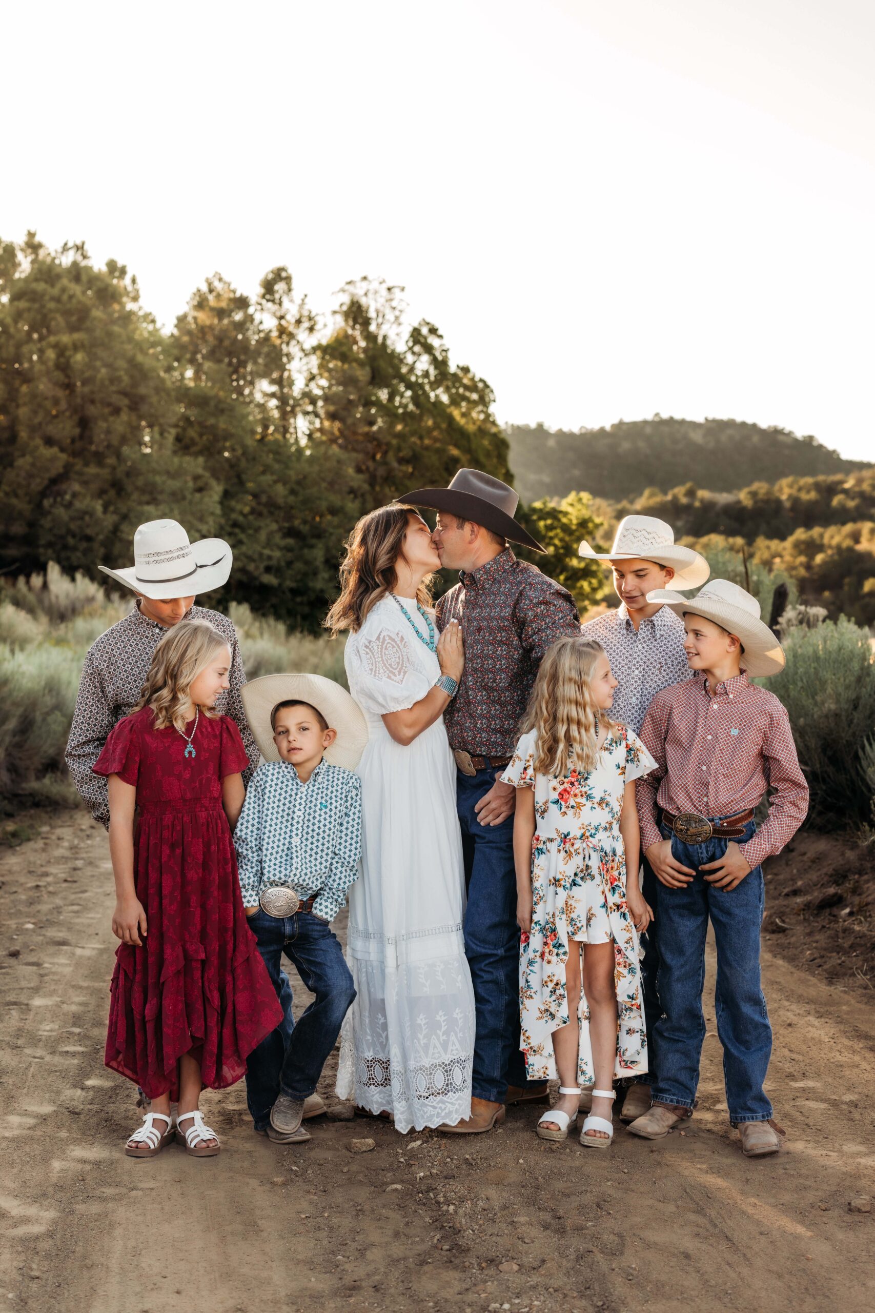 A family is dressed in western wear and cowboy hats while posing for a portrait in the country