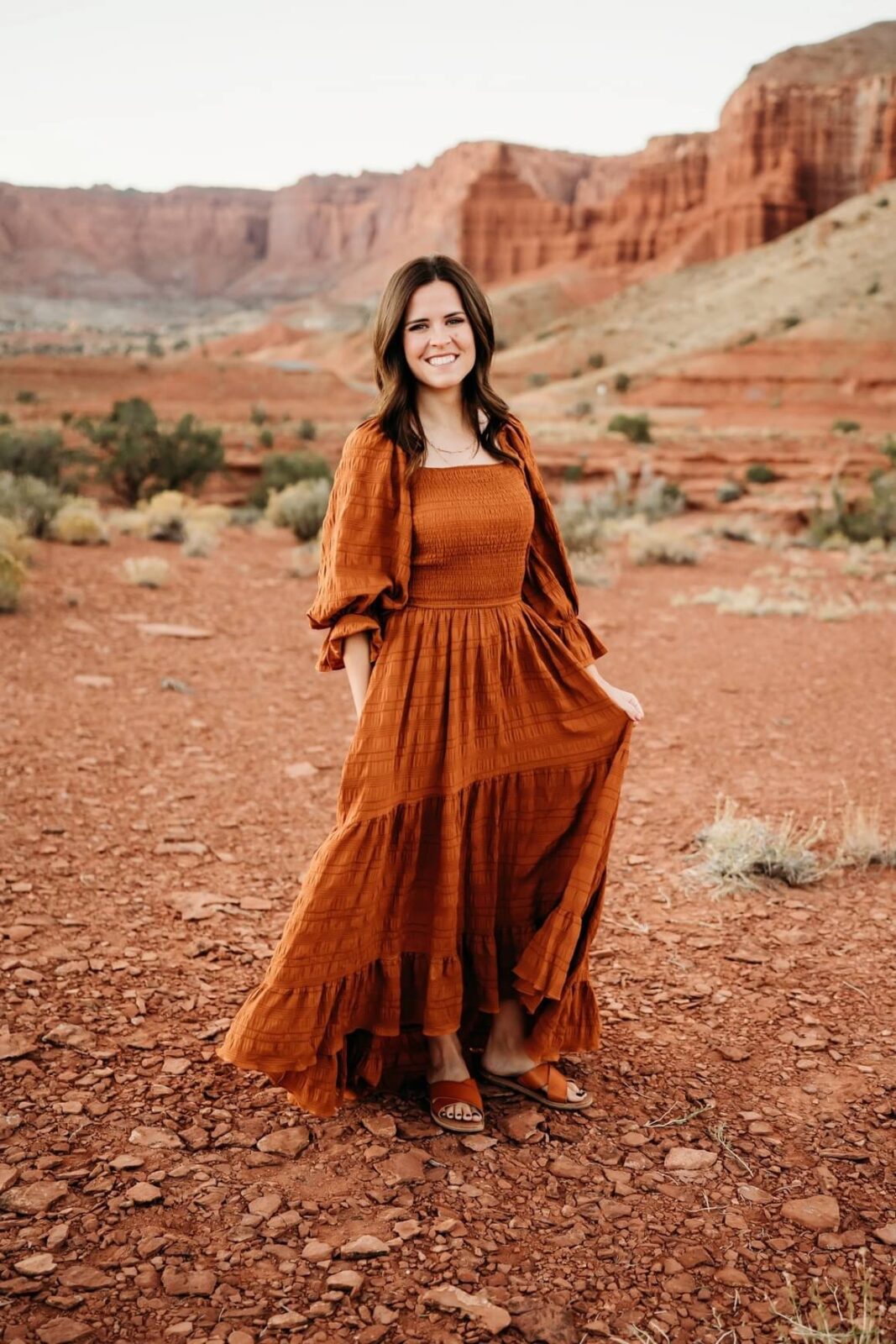 A woman stands in an orange dress against red rocks in southern utah
